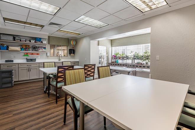 A spacious and well-lit community room with tables, chairs, and a kitchenette.