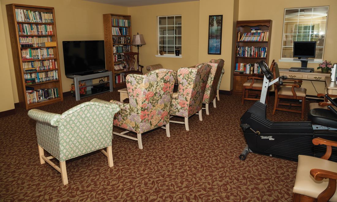 A cozy living room with floral armchairs, a large television, and filled bookshelves.