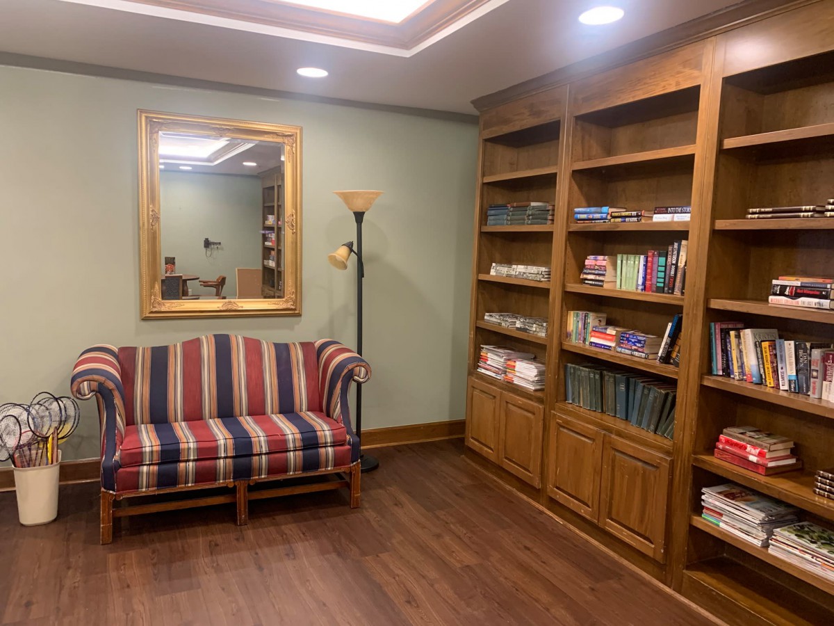 A cozy reading room with a striped sofa, wooden bookshelves filled with books, and a large mirror on the wall.