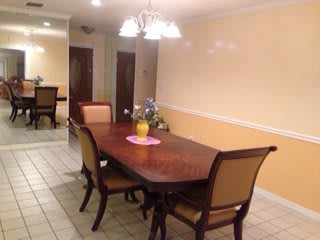 A well-lit dining room with a wooden table and six chairs under a chandelier.