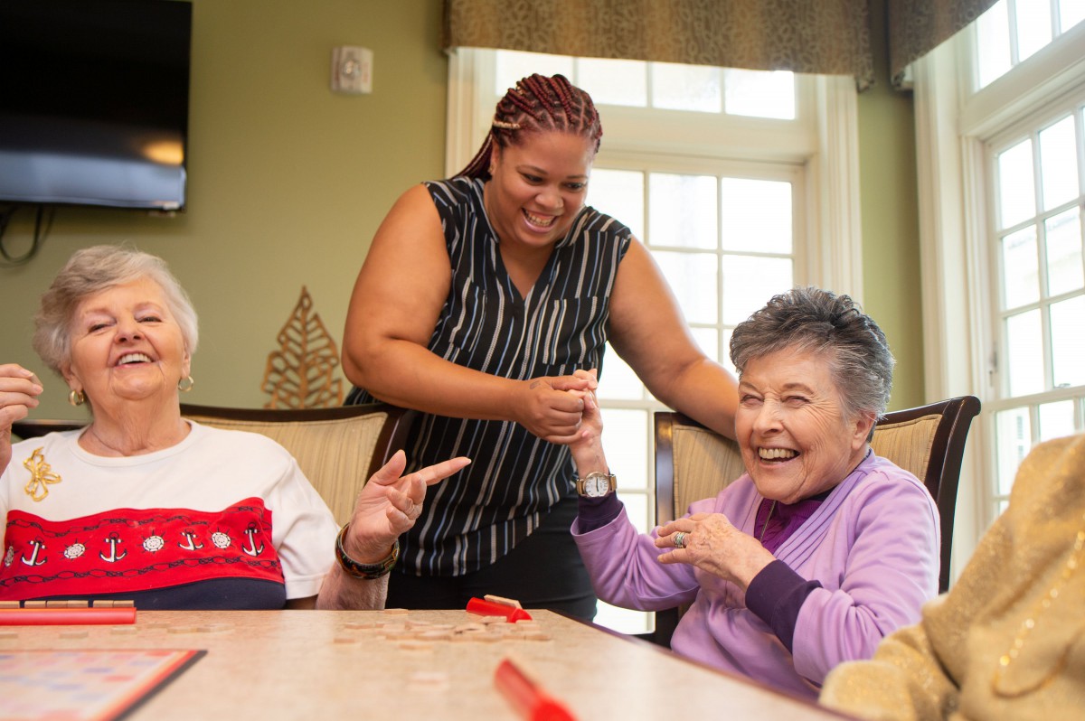 A caregiver interacting with two seniors, all sharing smiles and laughter indoors.