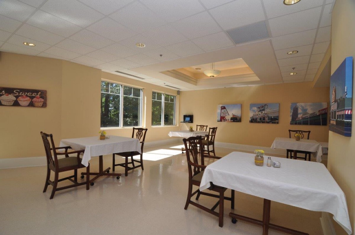 A modern dining room with several tables and chairs, illuminated by natural daylight through large windows.