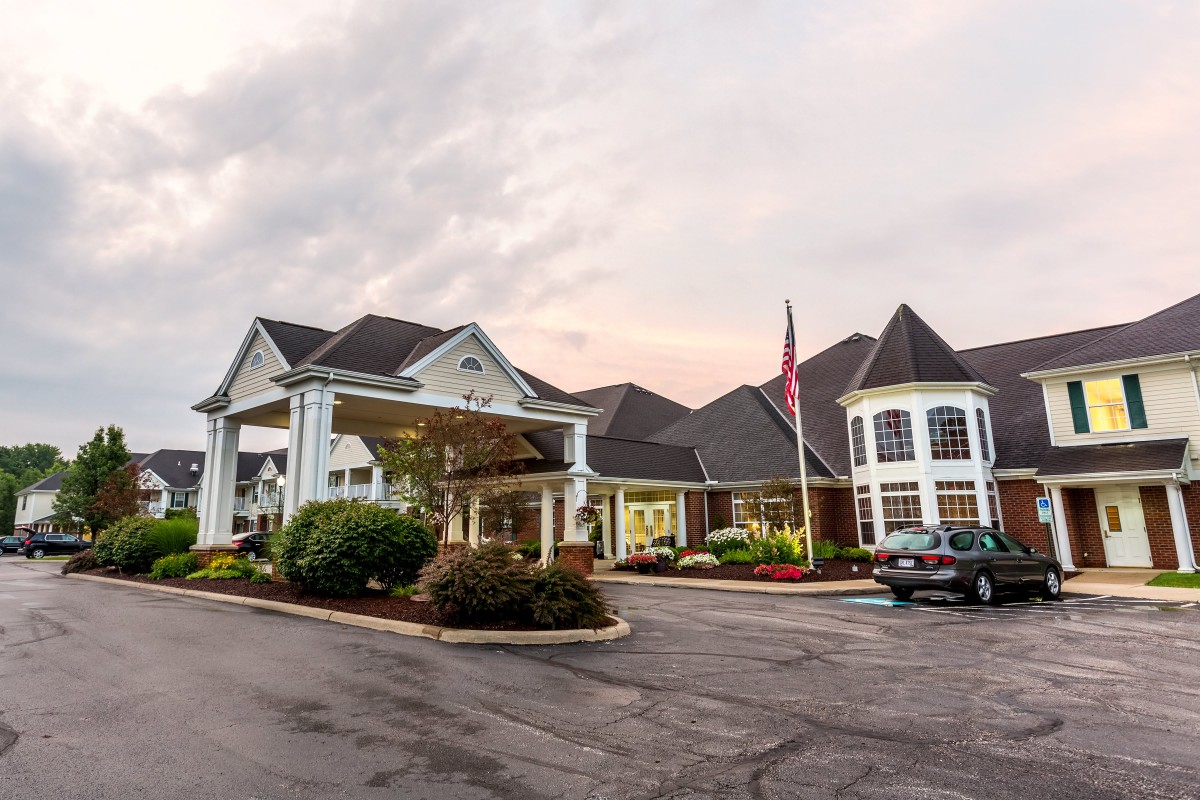 A hotel entrance with a driveway and parked car under a cloudy sky.