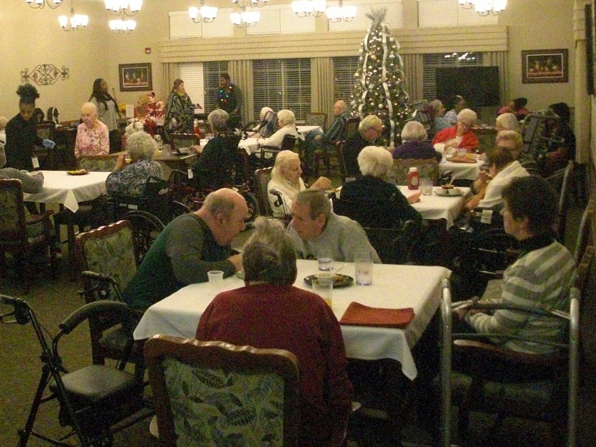 A group of elderly people gathered in a dining room decorated with a Christmas tree.
