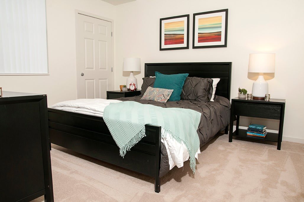 A cozy bedroom with a modern design, featuring a dark bed frame, colorful throw pillows, and abstract artwork on the walls.