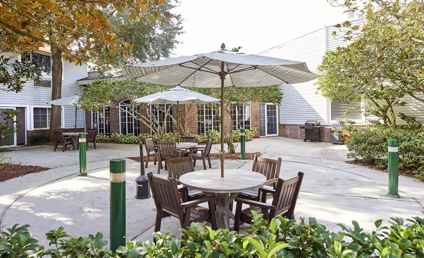 A peaceful outdoor patio area with tables, chairs, and umbrellas surrounded by greenery.