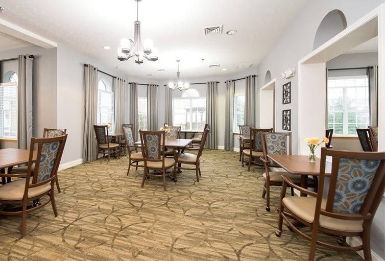 A bright and elegant dining room with multiple tables and chairs, overhung by chandeliers.