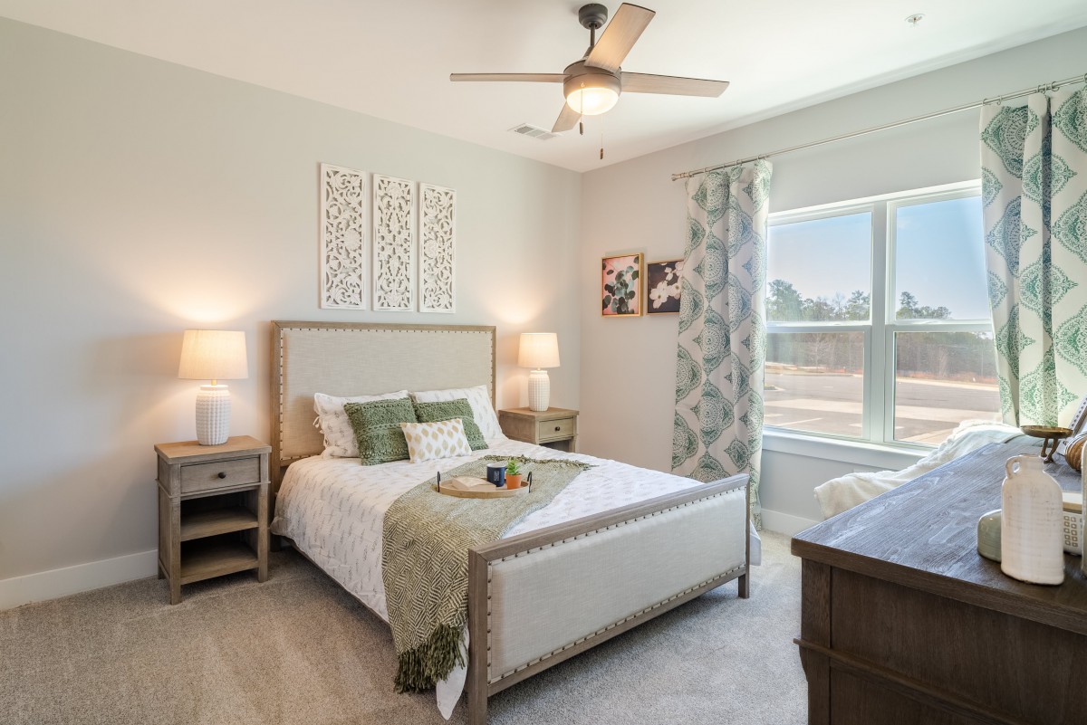 A cozy and well-decorated bedroom featuring a bed with green accents, nightstands with lamps, and a large window with patterned curtains.