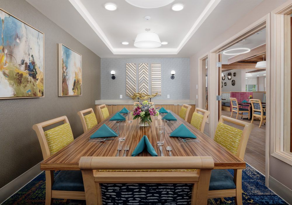 A modern dining room with a well-set table, adorned with teal napkins and floral centerpieces.
