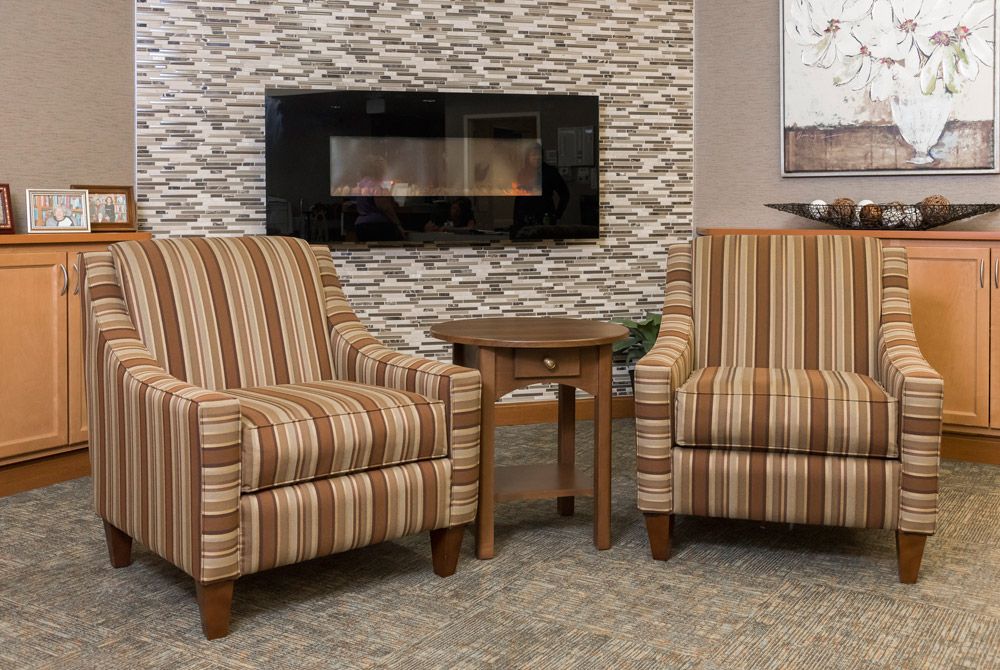 A cozy living room setting with two striped armchairs flanking a small side table, set in front of a modern fireplace.
