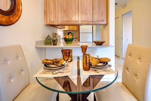 A beautifully arranged dining area featuring a glass table set for a meal, complemented by wooden kitchen cabinets and decorative items.