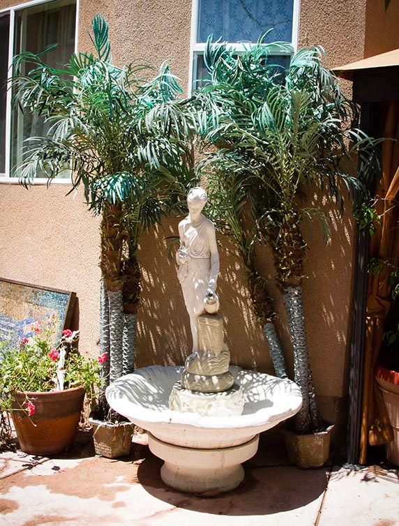 A decorative garden fountain with a statue surrounded by palm trees and potted plants.
