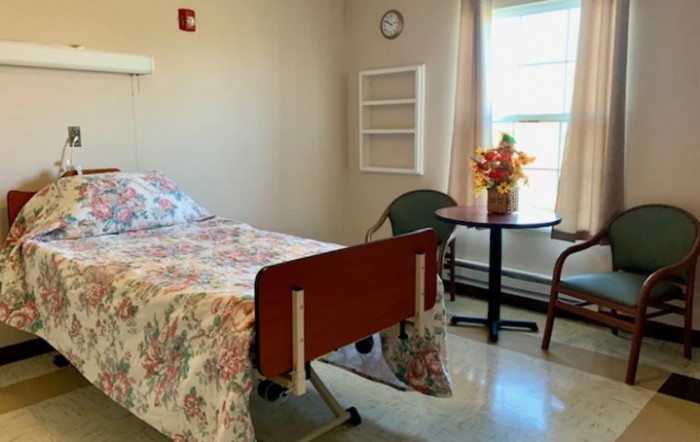 A well-lit hospital room with a single bed, chair, and flowers by the window.
