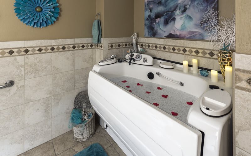A cozy bathroom with a bathtub filled with water and rose petals, flanked by candles and decorative elements.