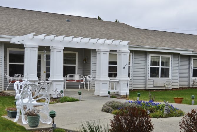 A suburban house with a white pergola over the front porch and landscaped front yard.