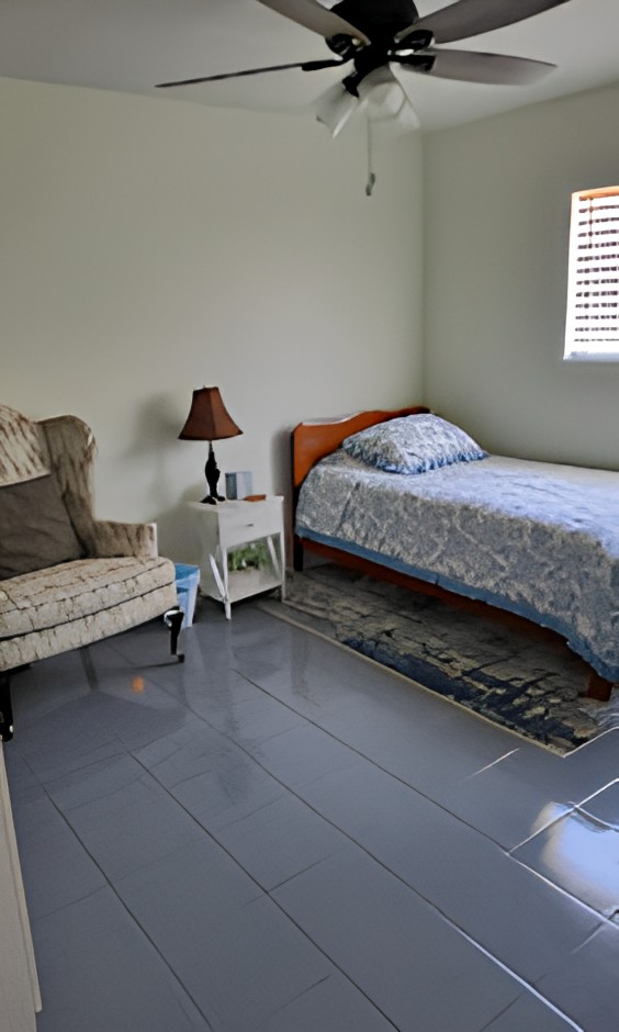 A simple bedroom with a single bed, armchair, and nightstand.