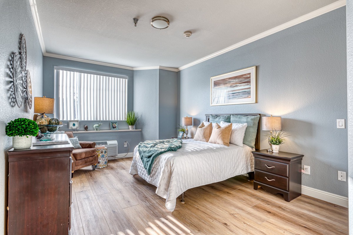 A modern and cozy bedroom with light blue walls, featuring a comfortable bed, stylish decor, and ample natural light from a large window.