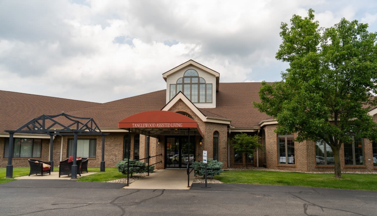 A building with a red-roofed entrance and brick exterior under a cloudy sky, surrounded by trees.