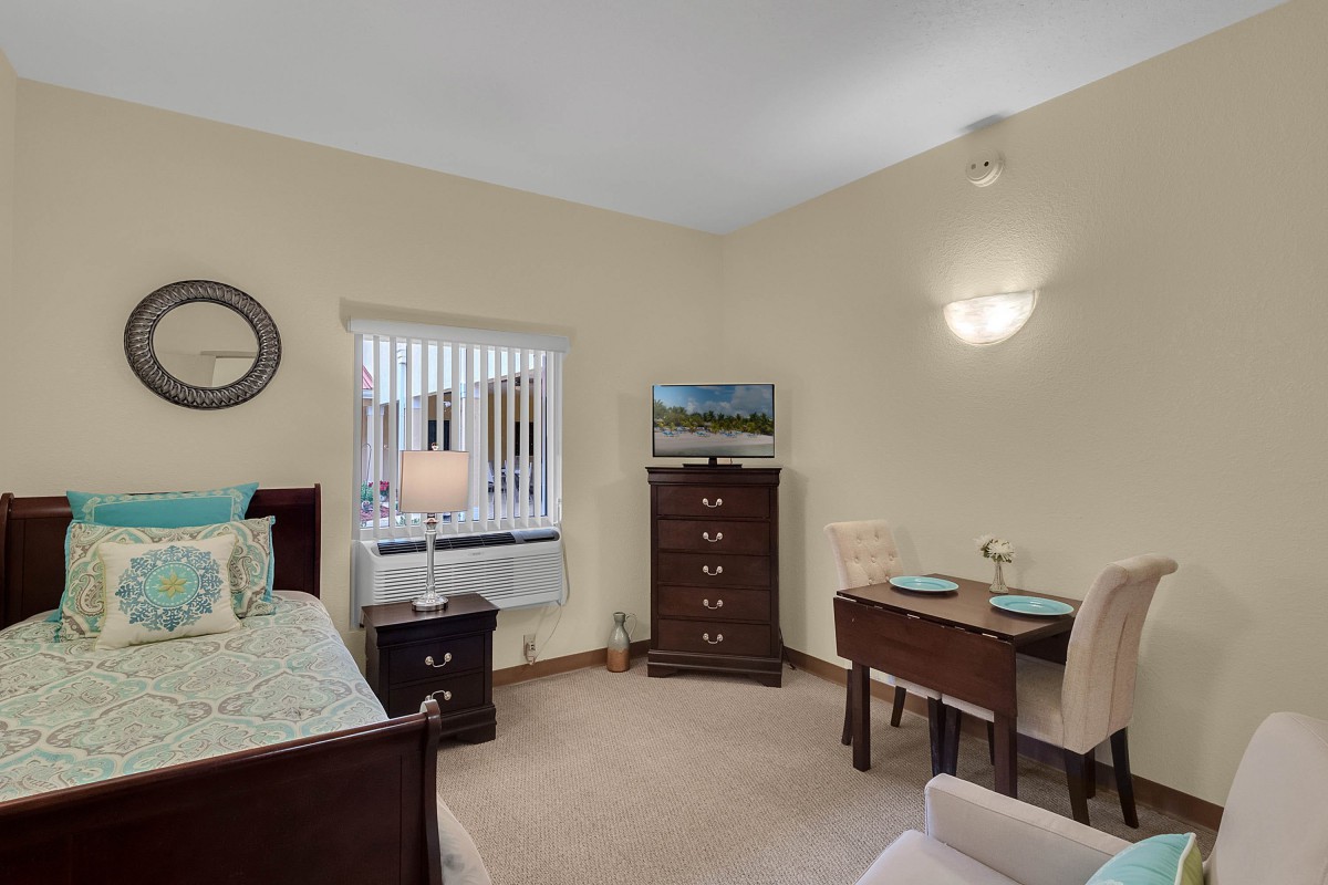 A cozy bedroom with a bed, dresser, and a small dining table set near a window.