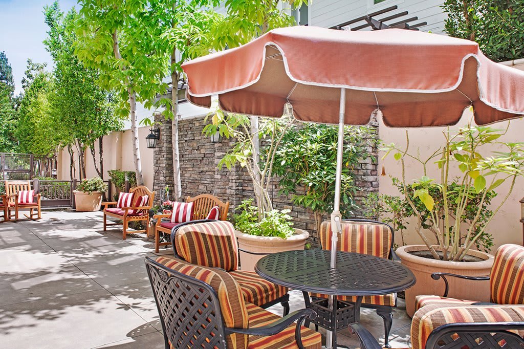 A cozy outdoor patio with striped cushioned chairs and a large umbrella.