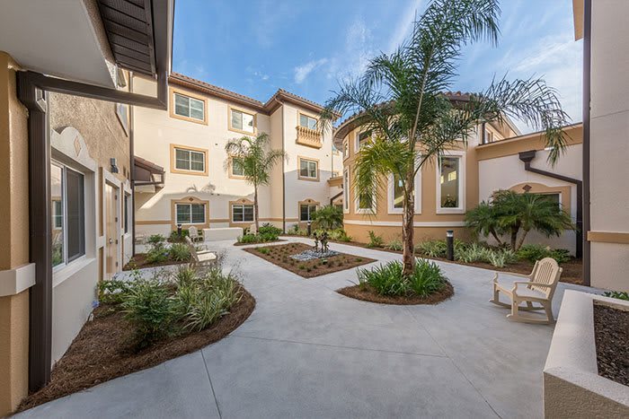 A spacious outdoor courtyard with landscaped gardens and palm trees surrounded by a multi-story building.