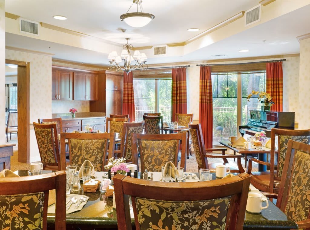A warmly lit dining room with elegantly decorated tables and chairs, featuring large windows and elegant chandeliers.