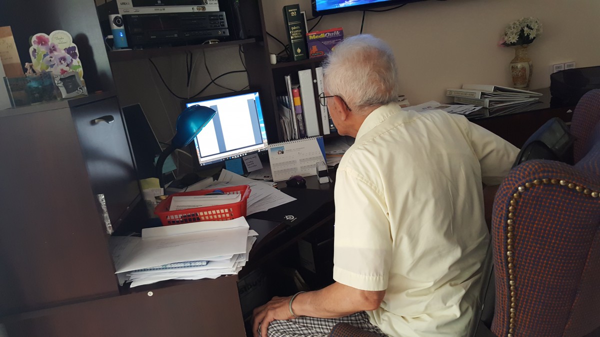 An elderly person working at a computer in an office setting.