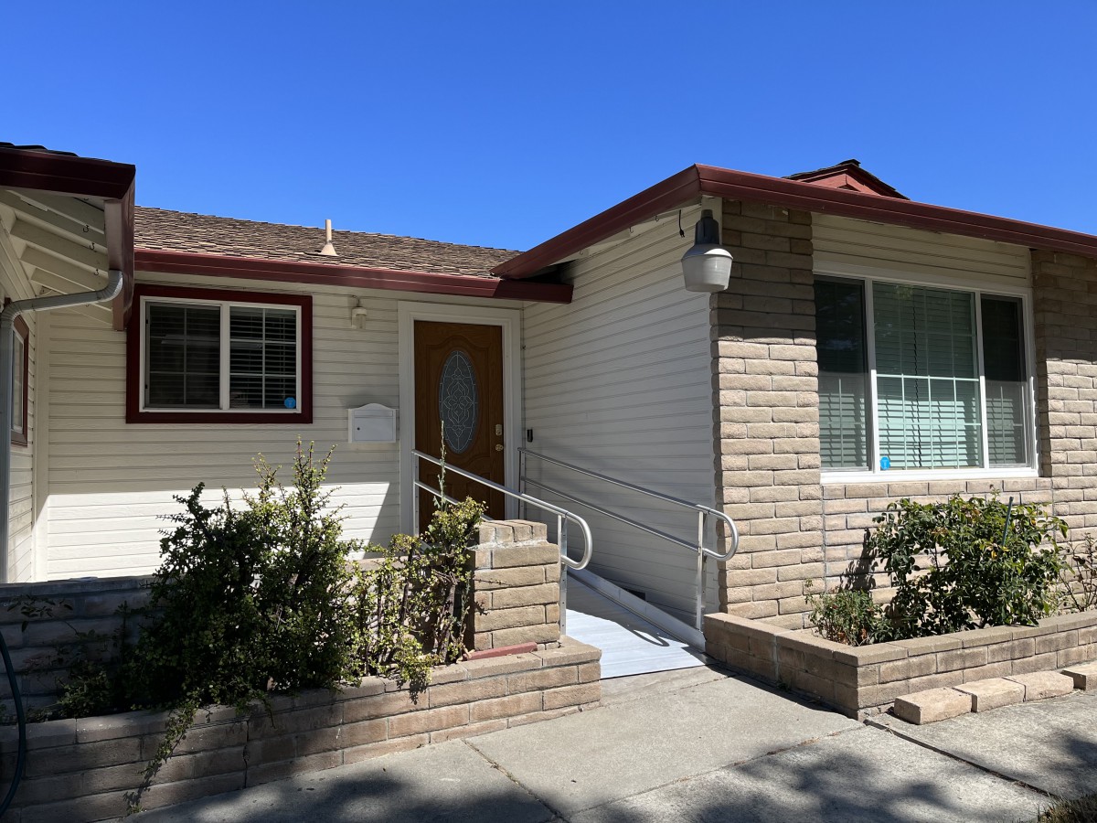 A suburban house with a front entrance ramp and brick facade under a clear blue sky.