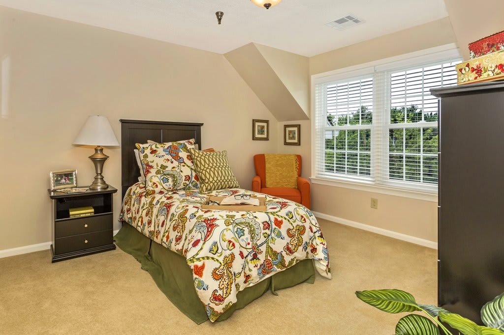 A cozy bedroom with a single bed, colorful bedding, and a large window allowing natural light in.