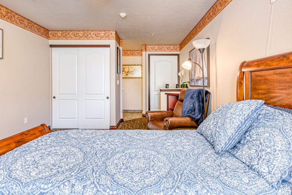 A cozy bedroom featuring a bed with patterned bedding, an armchair, and soft lighting.