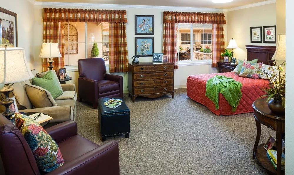 A cozy bedroom with comfortable seating, a bed with colorful bedding, and large windows allowing natural light.