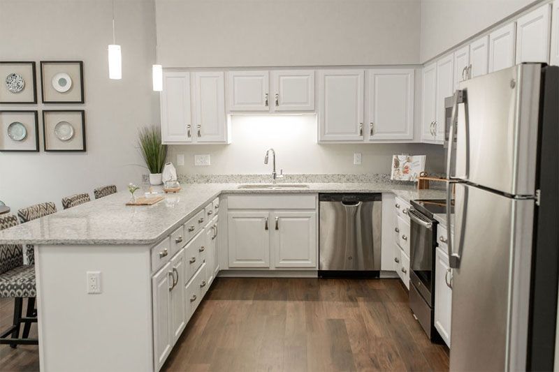 A modern kitchen featuring white cabinets, stainless steel appliances, and hardwood flooring.