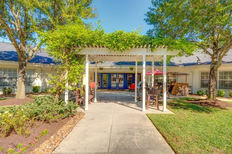 A welcoming entrance featuring a pergola-covered pathway surrounded by lush greenery and landscaping.