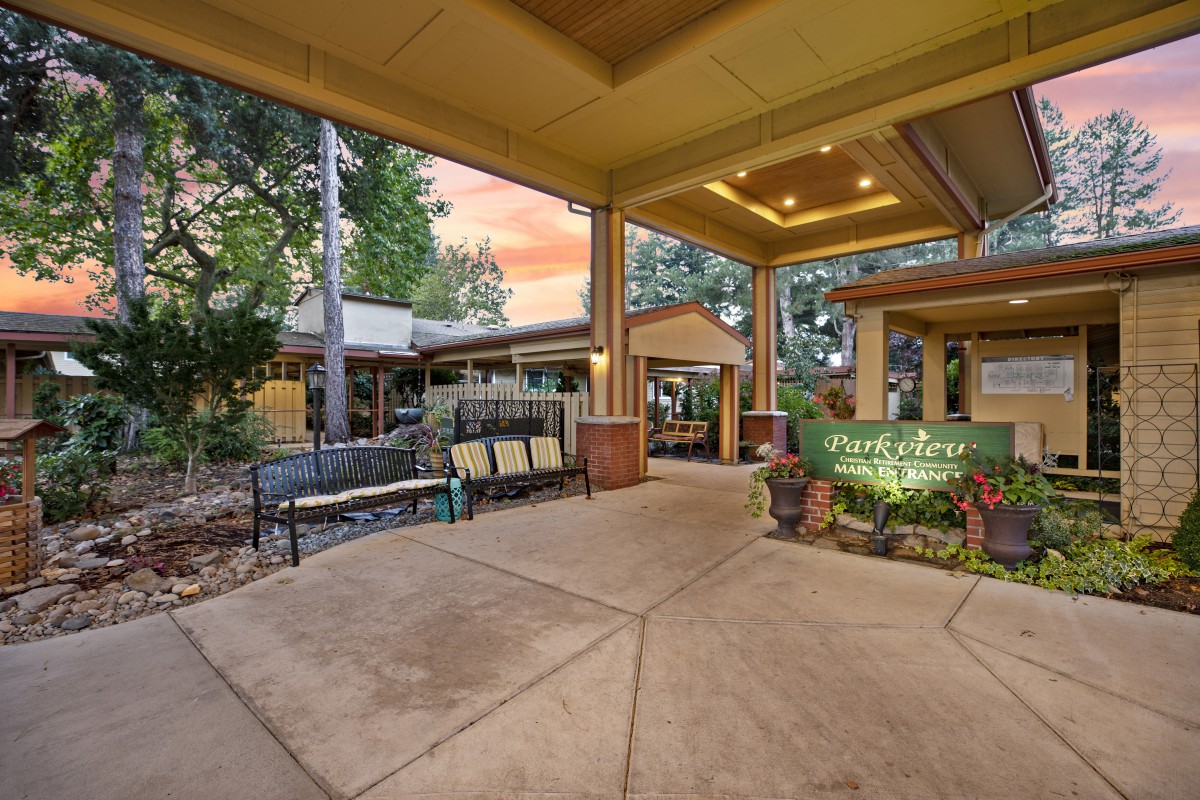 A welcoming entrance area featuring benches and plants under a covered walkway, set against an evening backdrop.
