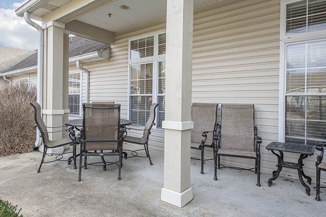 A cozy covered patio with a set of chairs and a table.