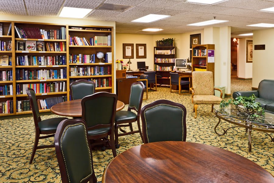 A cozy library room with bookshelves, tables, and chairs for reading.