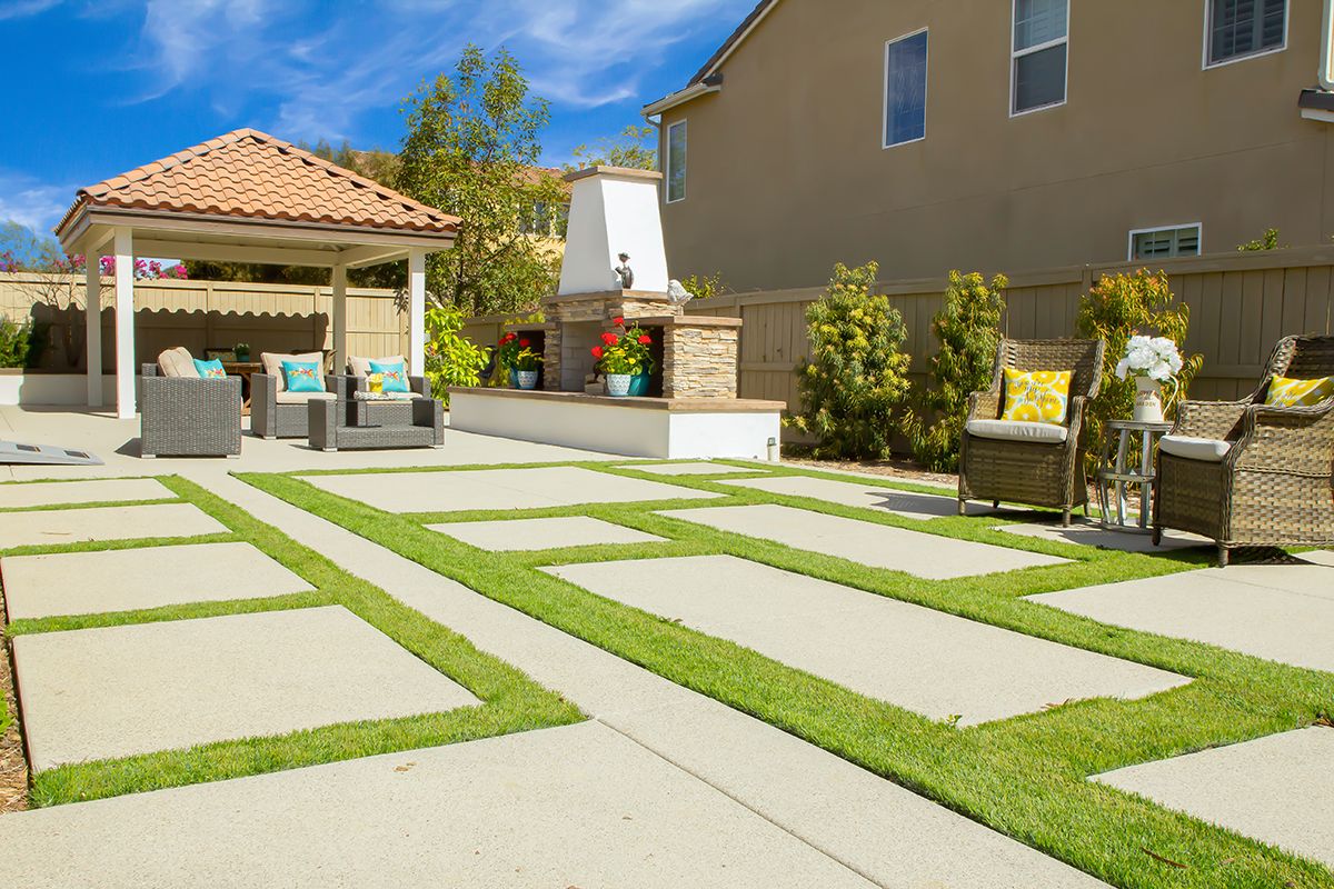 A well-maintained backyard with a patio, outdoor seating, and a paved walkway surrounded by lush greenery.