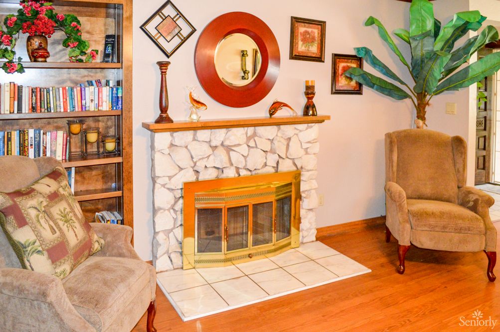 A cozy living room featuring a stone fireplace with decorative elements, a mirror, and comfortable seating.