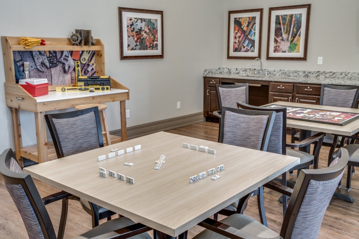 A cozy game room with a table set for dominoes, surrounded by chairs and decorated with colorful artwork.