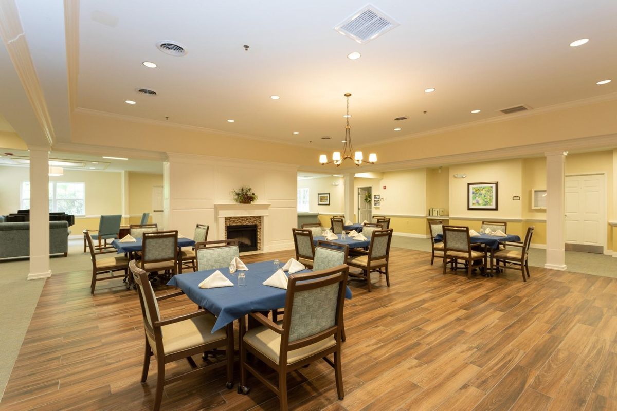 A cozy dining room with neatly arranged tables and chairs, featuring warm lighting and a wooden floor.