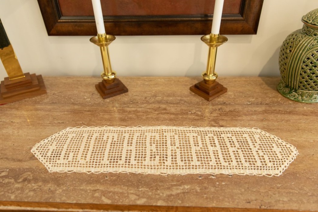 A decorative lace doily placed on a wooden table with two brass candlesticks.