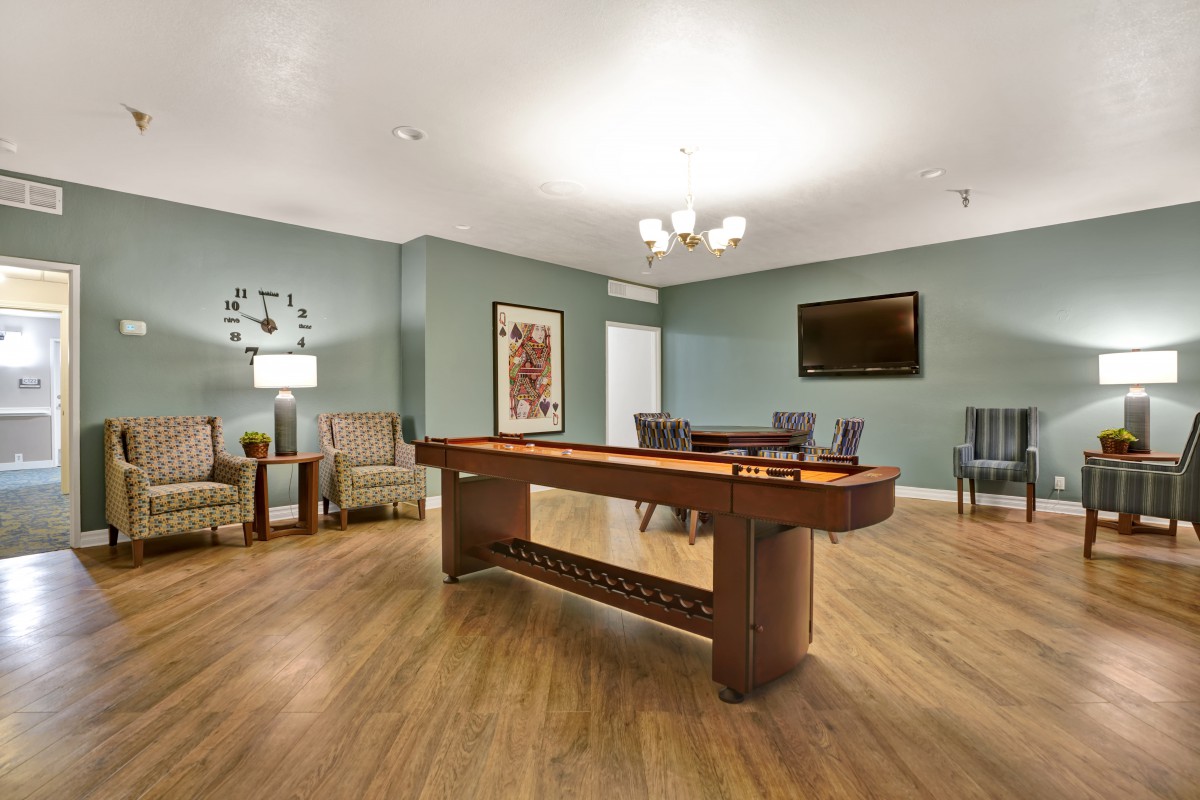 A modern game room featuring a shuffleboard table, seating area, and elegant decor.