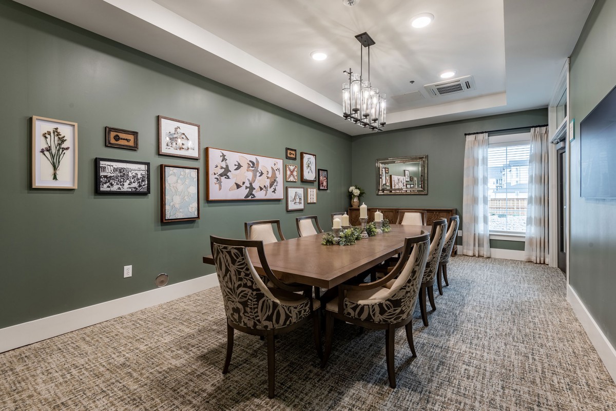 A well-furnished dining room featuring a long wooden table, patterned chairs, and decorative artwork on green walls.