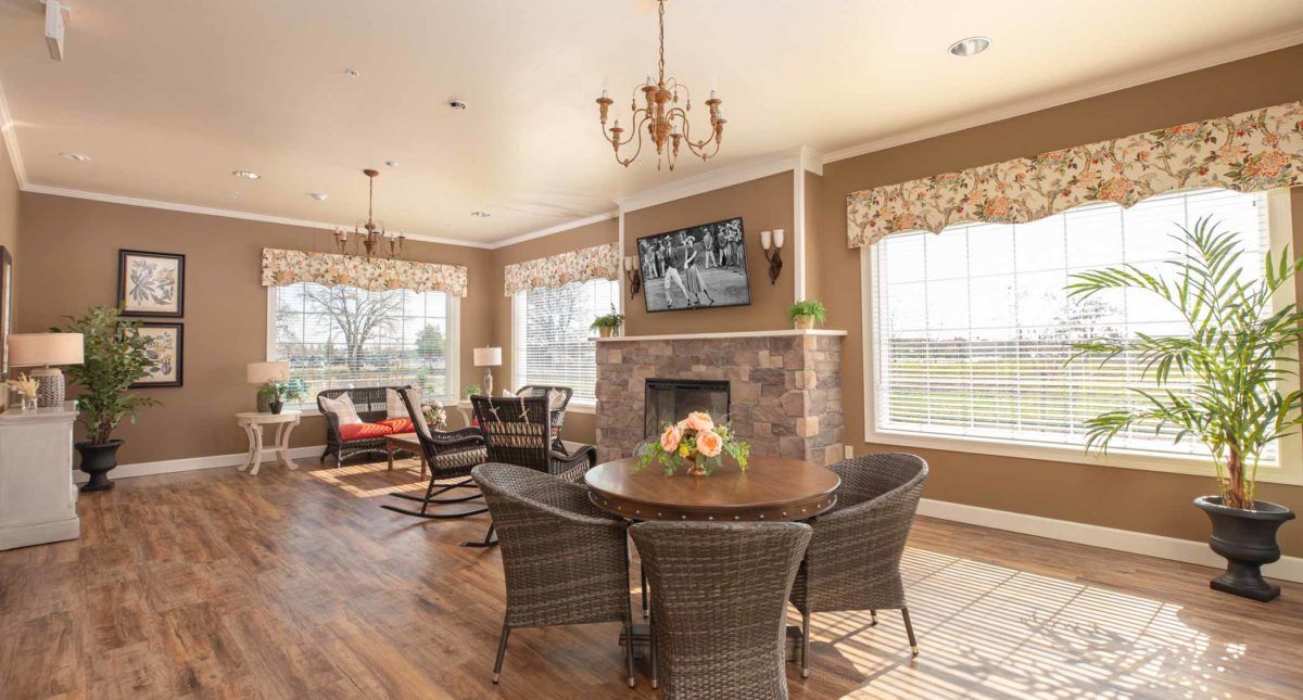 A cozy living room with a fireplace, television, and wicker chairs arranged around a wooden table.
