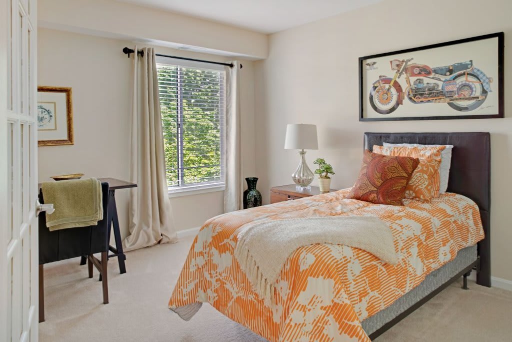 A cozy bedroom with orange floral bedding and natural light streaming through the window.