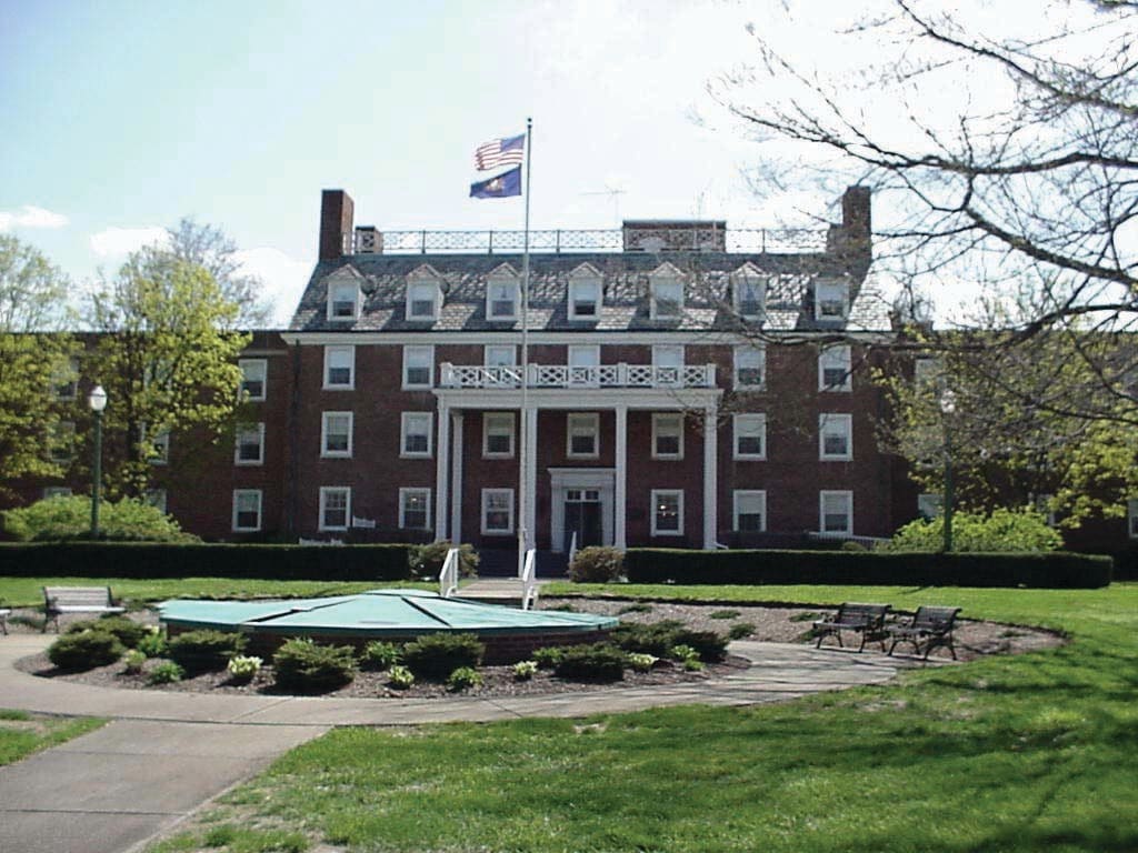 A brick building with a flag on top, surrounded by a well-maintained lawn and trees.