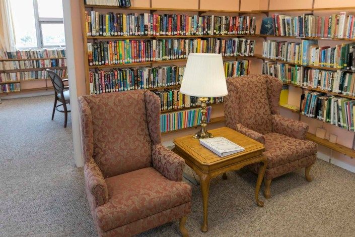 A cozy reading area in a library with bookshelves, two chairs, and a lamp on a table.