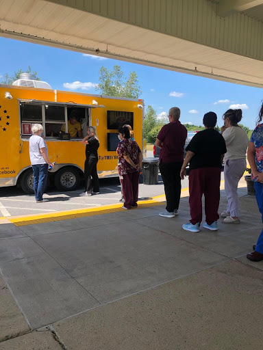 A group of people waiting in line at a food truck on a sunny day.