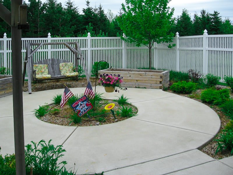 A well-maintained patio garden with various flowers and a white fence.