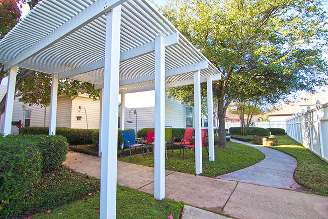 A backyard patio area with a white pergola and colorful chairs.